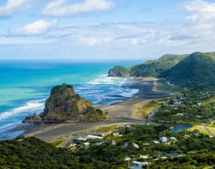 Coastal view of Piha Beach, New Zealand with Lion Rock and surrounding green hills.