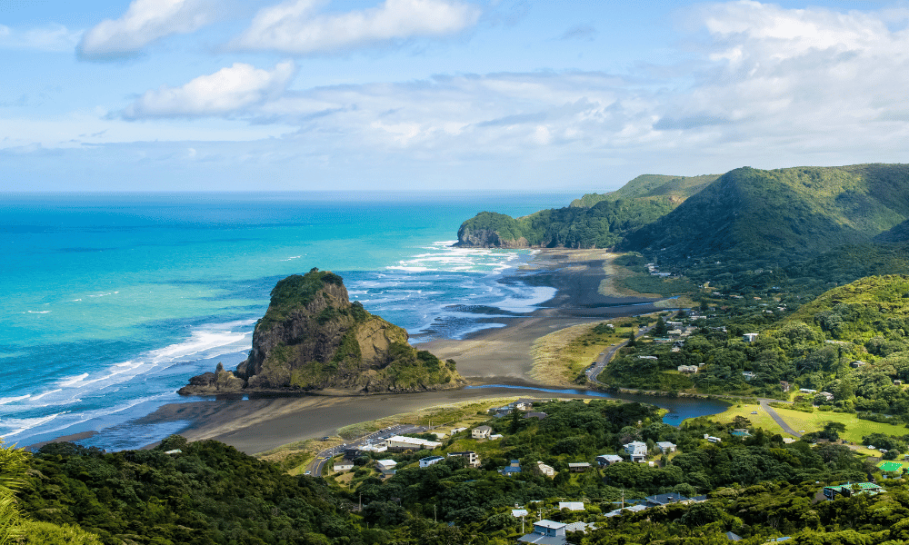 Coastal view of Piha Beach, New Zealand with Lion Rock and surrounding green hills.