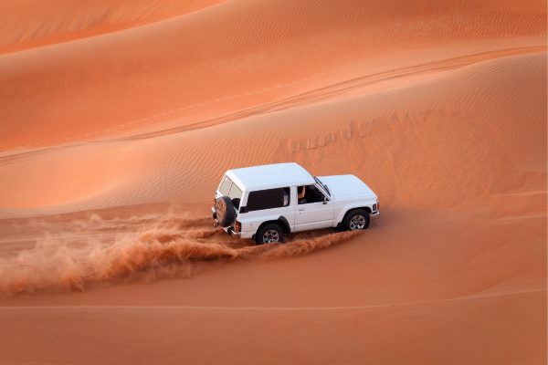 White 4x4 vehicle driving over orange sand dunes in the Dubai desert.