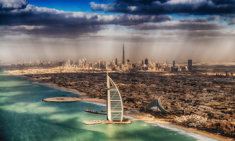 Aerial view of Dubai’s coastline featuring the Burj Al Arab hotel, turquoise waters, sandy beaches, and the city skyline with the Burj Khalifa